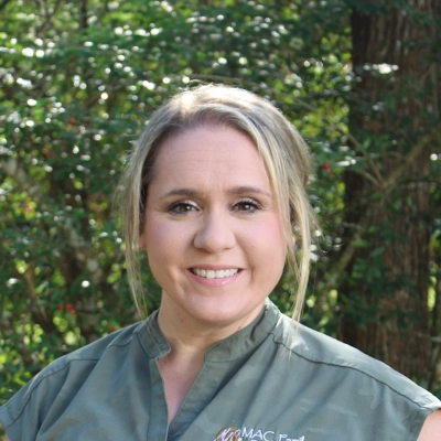Office Manager Alicia Winslow Smiling Outdoors In Front Of Greenery