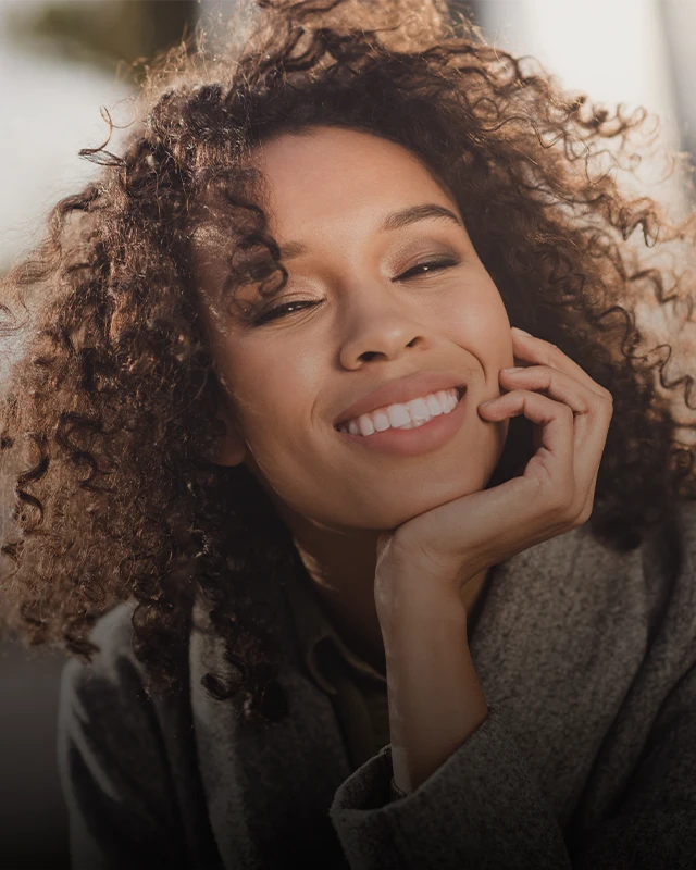 A young woman resting her chin in her hand and smiling, showing straight white teeth