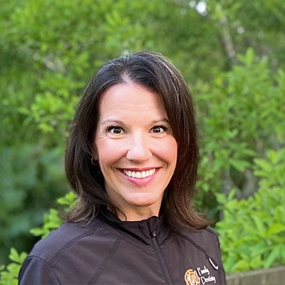 Dental Hygienist Valerie Mouille Daniel Smiling Outdoors In Front Of Greenery